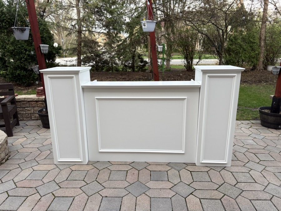 A white panelled event bar with matching pedestals on a paver patio
