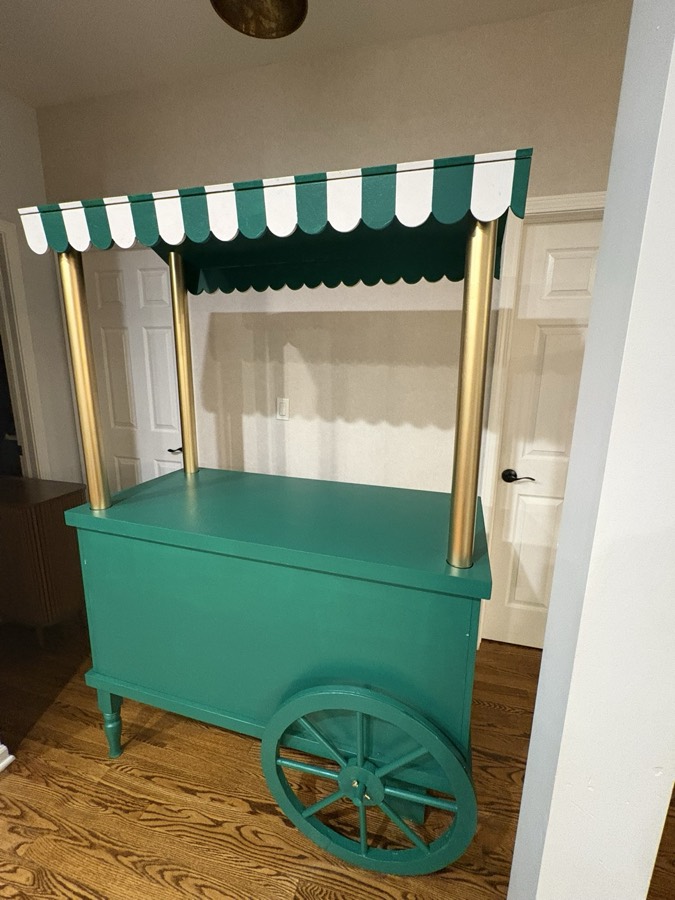A teal candy cart with a scalloped green-and-white awning and brass poles