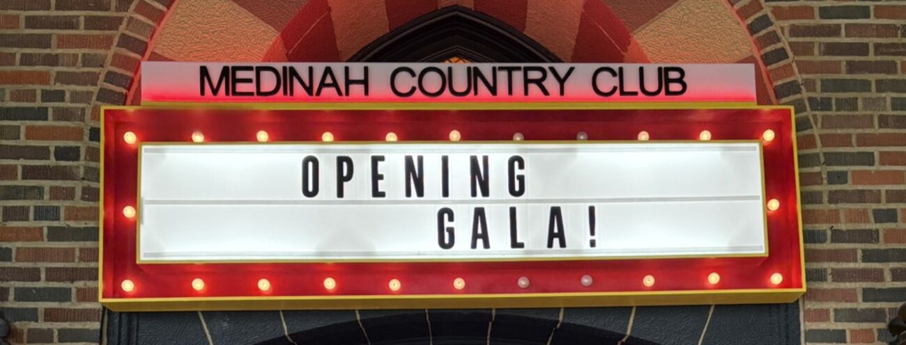 A lit marquee sign built by MH Build Studio, mounted on brickwork above a country-club entrance and reading OPENING GALA
